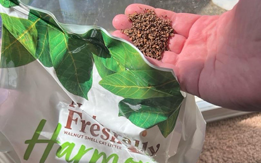 Hand holding walnut litter next to Naturally Fresh Harmony bag